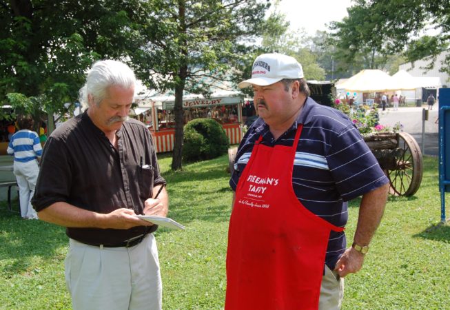 John Golden, a journalist covering folklife, visits Freeman's Taffy Stand, a North Country Living Traditions Very Special Place award recipient, at the Lewis County Fair. Date and photographer unknown.